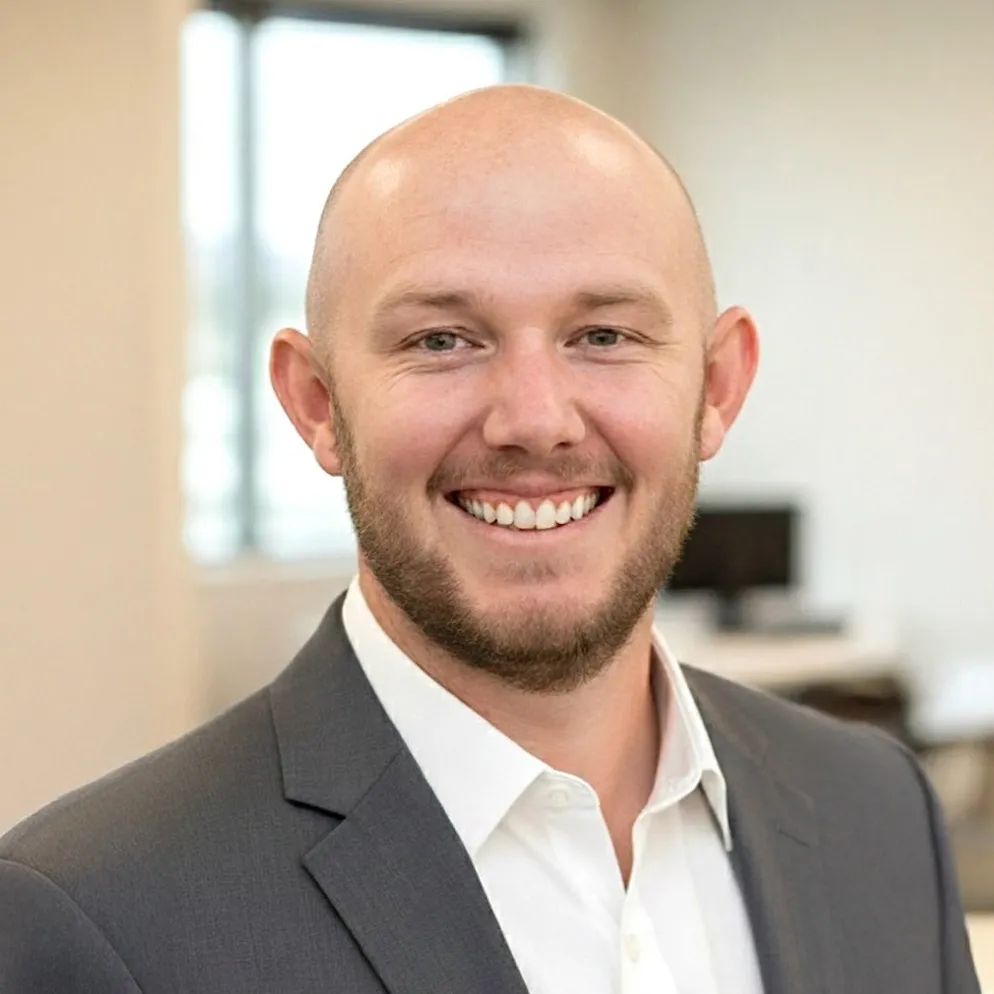 Professional headshot of a smiling man in a charcoal suit jacket and white shirt.