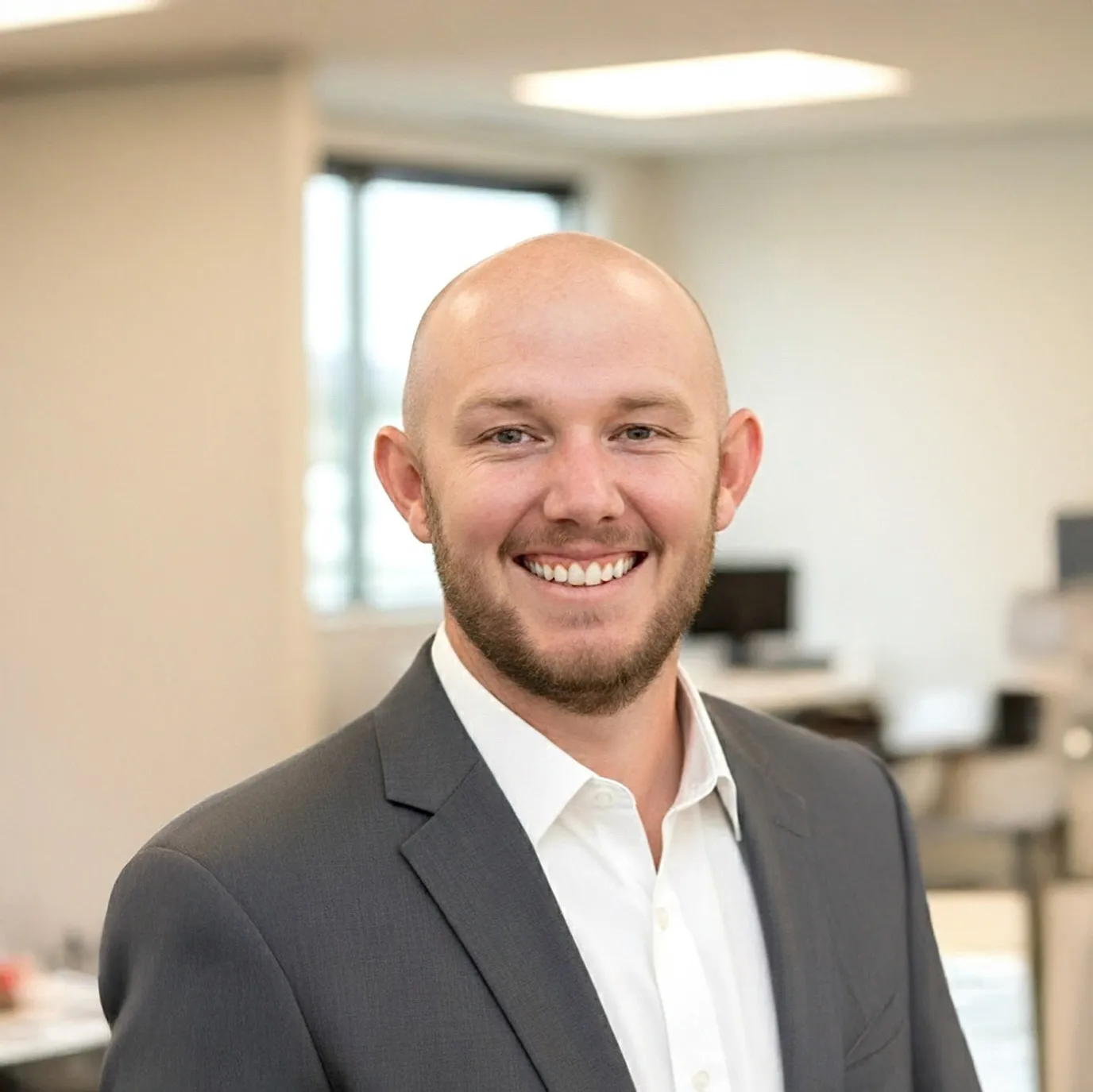 Professional headshot of a smiling man in a dark suit jacket and white shirt in a modern office setting.